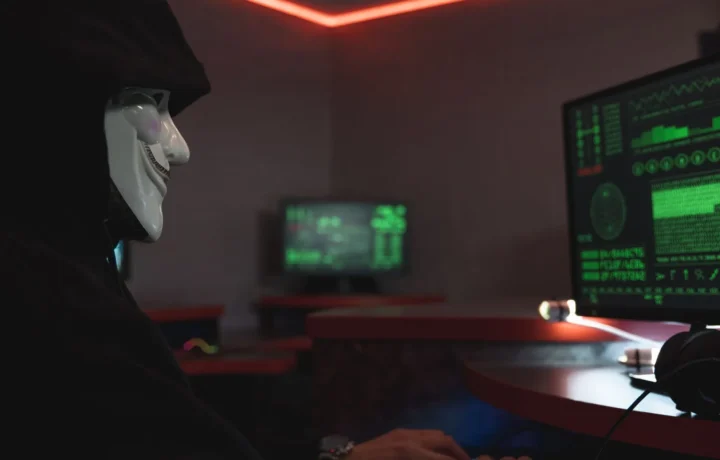 Hacker mascarado diante de um monitor em sala escura, representando a ameaça que a API anti-fraude ajuda a bloquear