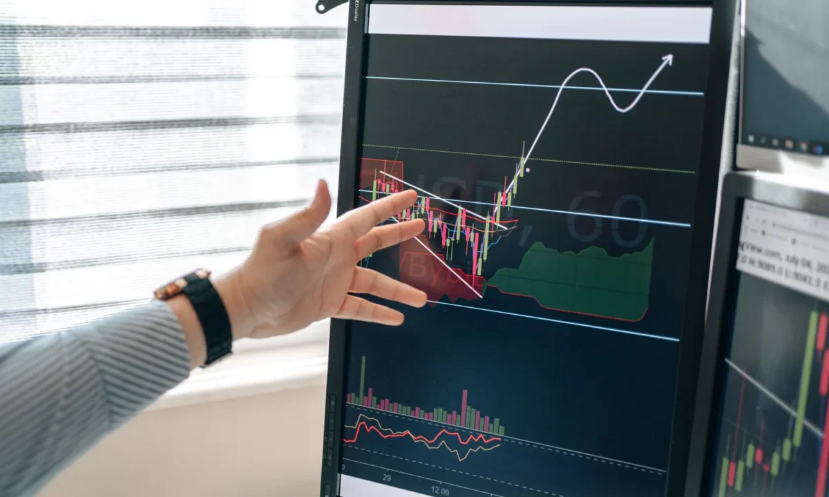 Mão apontando para gráficos financeiros em um monitor, ilustrando o algoritmo de fraude de pagamento analisando transações