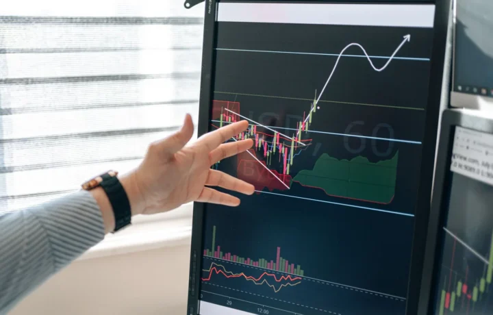 Mão apontando para gráficos financeiros em um monitor, ilustrando o algoritmo de fraude de pagamento analisando transações