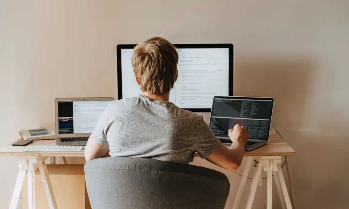 Adolescente programando com vários laptops em espaço de trabalho moderno, representando aprendizado máquina contínuo