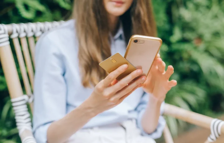 Mulher faz uma compra online com celular e cartão, utilizando pix link de pagamento ao ar livre